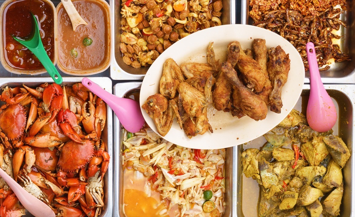 Variety of delicious Malaysian home cooked dishes sold at street market stall in Kota Kinabalu Sabah from top angle view with seller in motion taking food.